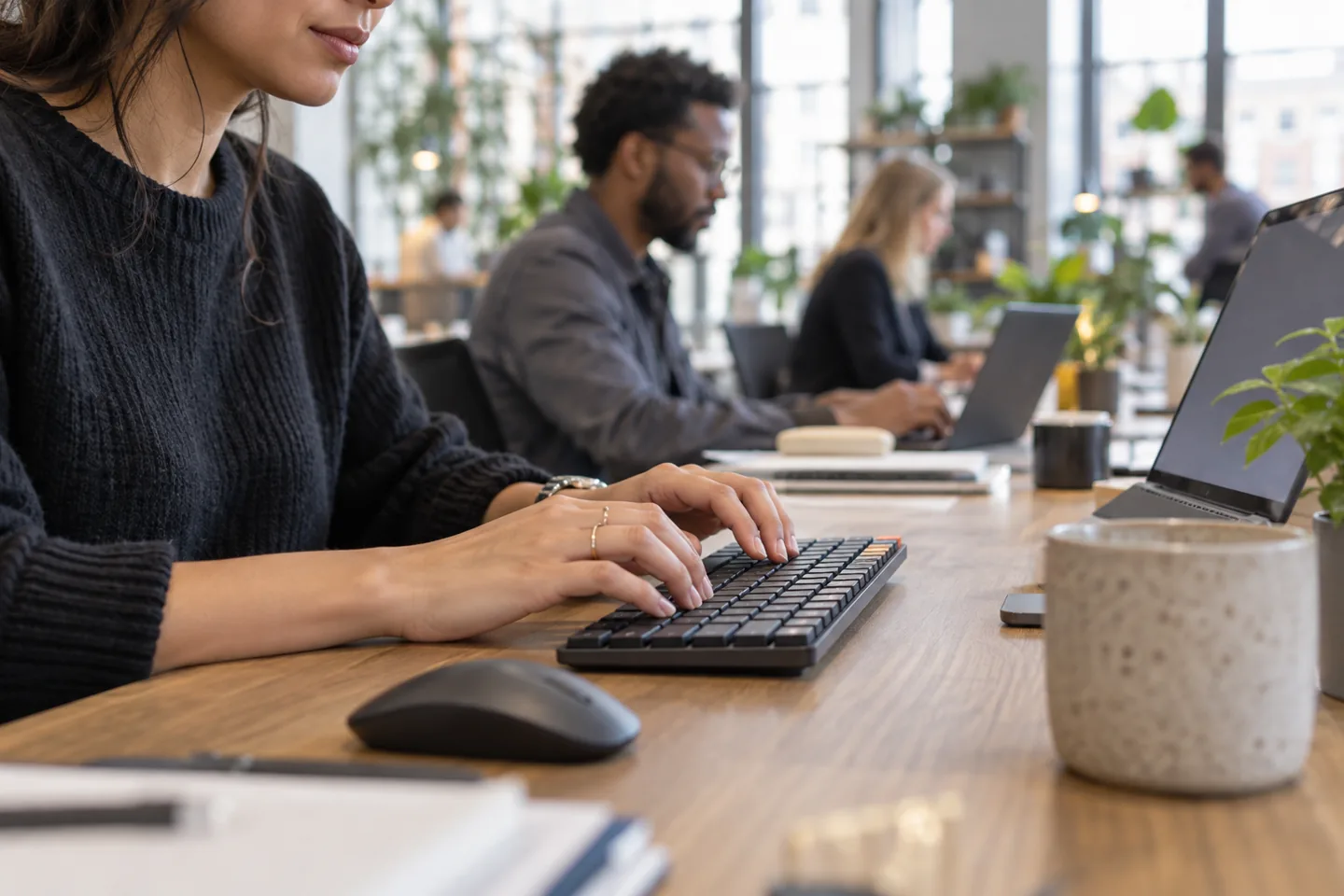 A professional typing on a low-profile mechanical keyboard in a shared coworking space.